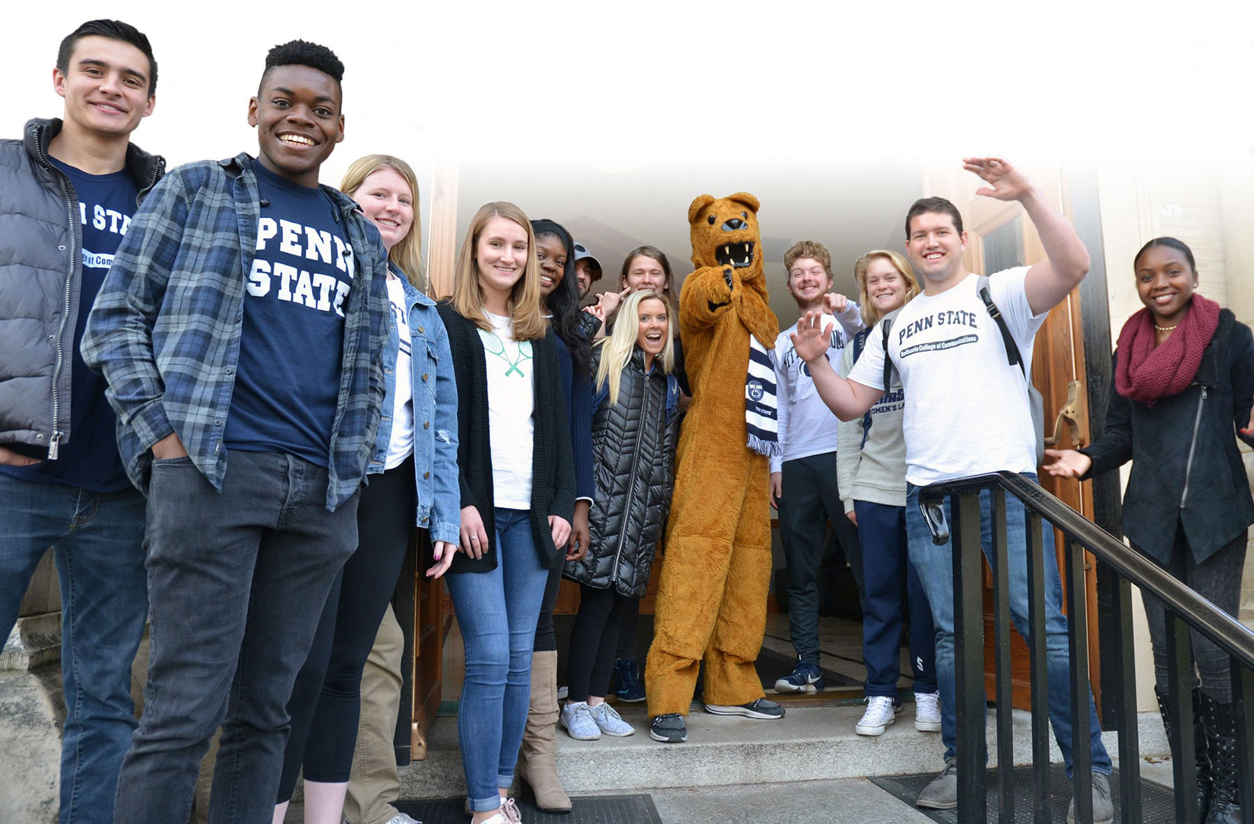 The Nittany Lion mascot points his finger at the camera while posing with a bunch of students on the Carnegie Building steps