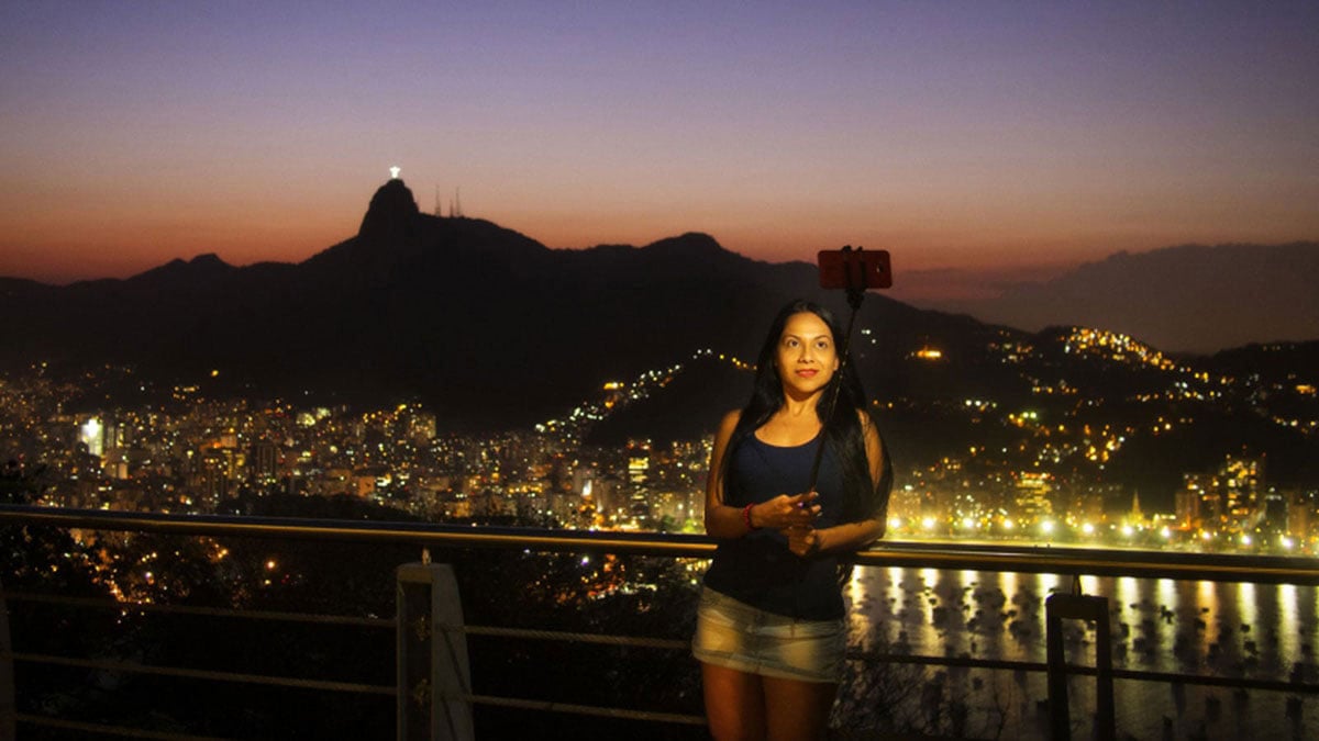 A Student captures a selfie as the sun sets in Rio with the cityscape behind