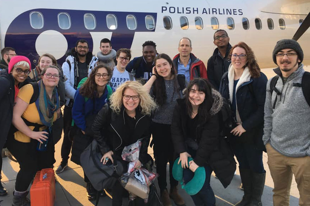 A mixed group of faculty and students on an international course experience pose in front of a Polish Airlines jet.