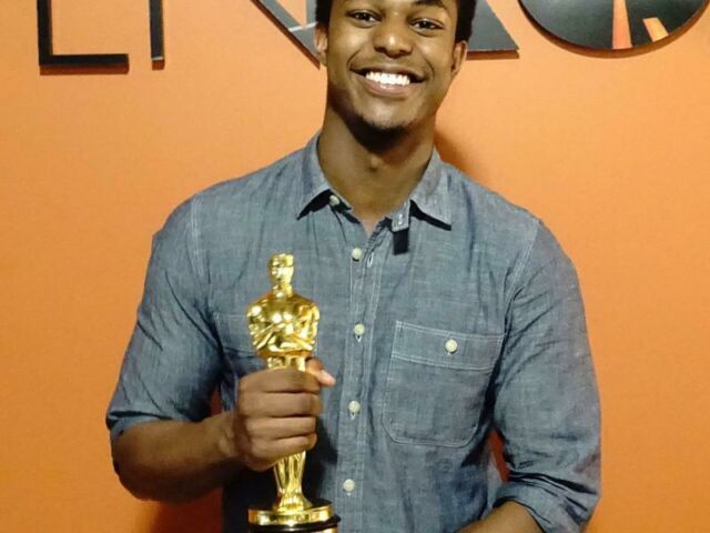 Penn State student Carl LaGuerre holding an Oscar trophy in front of an orange background