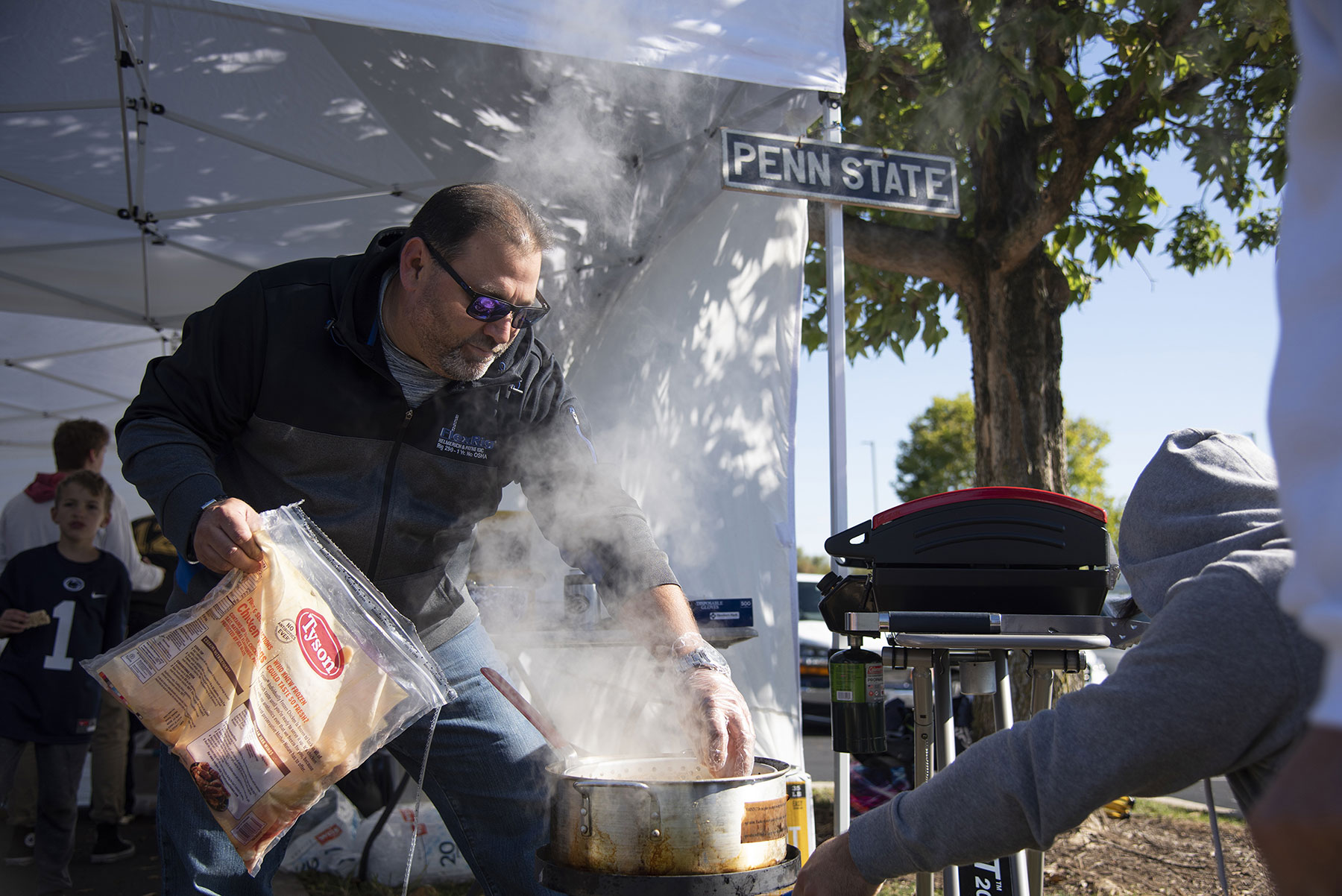 A tailgater prepares to throw a big bag of chicken wings into a deep fryer.
