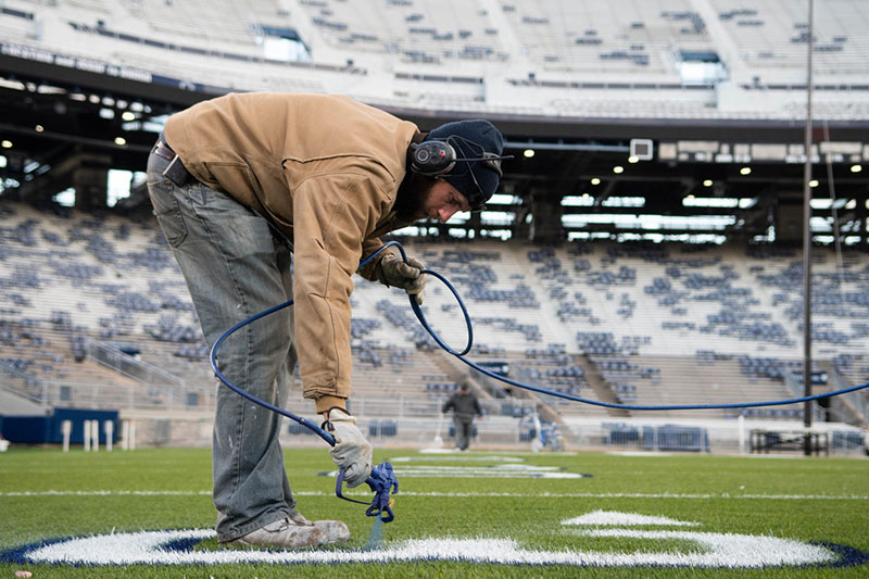 A groundskeeper yields a paint sprayer and puts down yard lines.