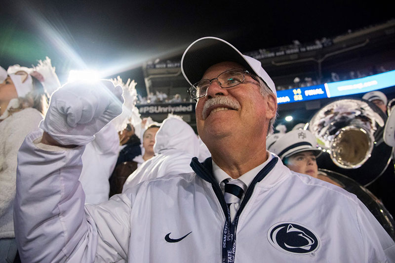 Dave Cree dressed in a white Penn State jacket and baseball hat pumps his fist to celebrate a touchdown.