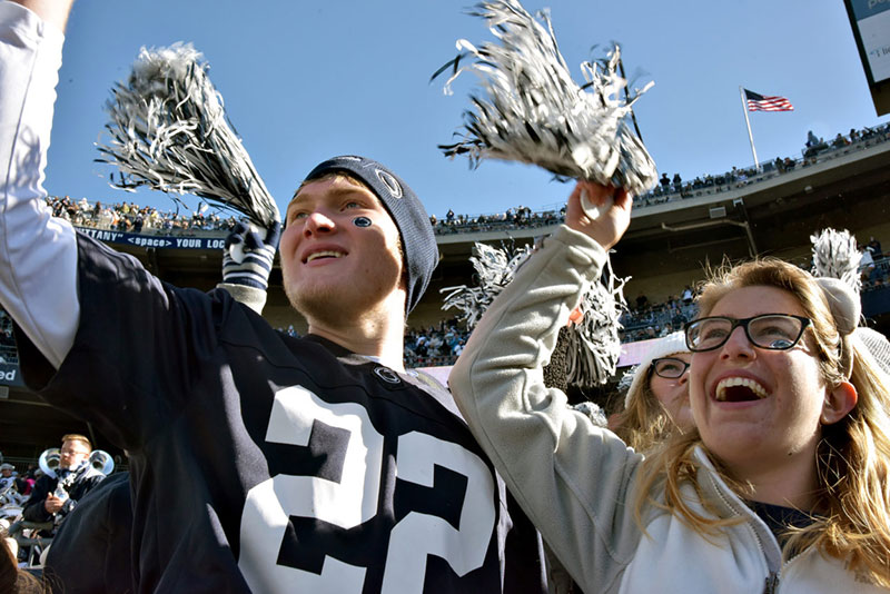 Fans raise blue and white pom poms as they cheer on the Penn State football team.