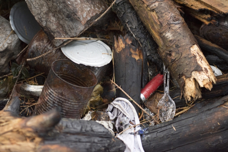 Burnt cans, wood, and other trash sit in a fire pit.
