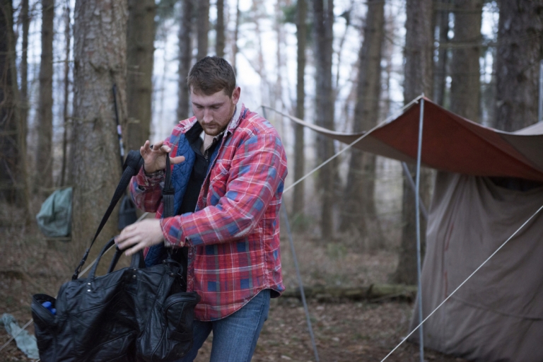 Zack dressed in a red flannel shirt jacket carries a black duffel bag.