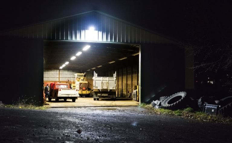 A work shed lit up at night with Zack working inside on an old red, 1968 International pickup truck